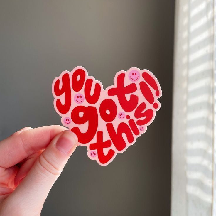 Heart-shaped sticker with 'you got this!' text held by a hand against a neutral background